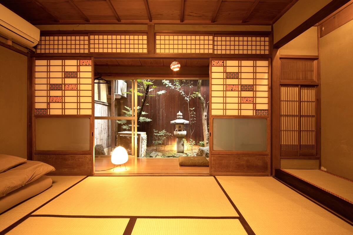 A traditional Japanese room with tatami flooring, sliding doors, and a view of a garden with a stone lantern.