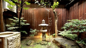A traditional Japanese garden with a stone lantern, moss-covered rocks, and a wooden fence. - Guesthouse YULULU (Kyoto)