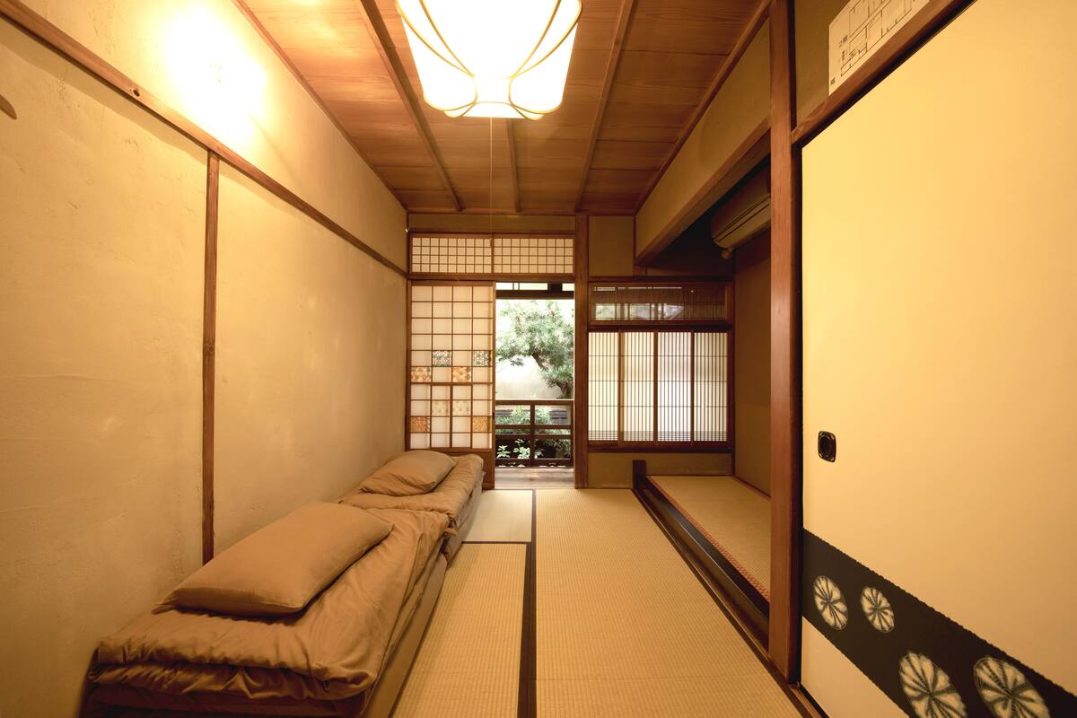 A traditional Japanese room with tatami flooring, a low wooden bed, and a sliding door leading to a garden.
