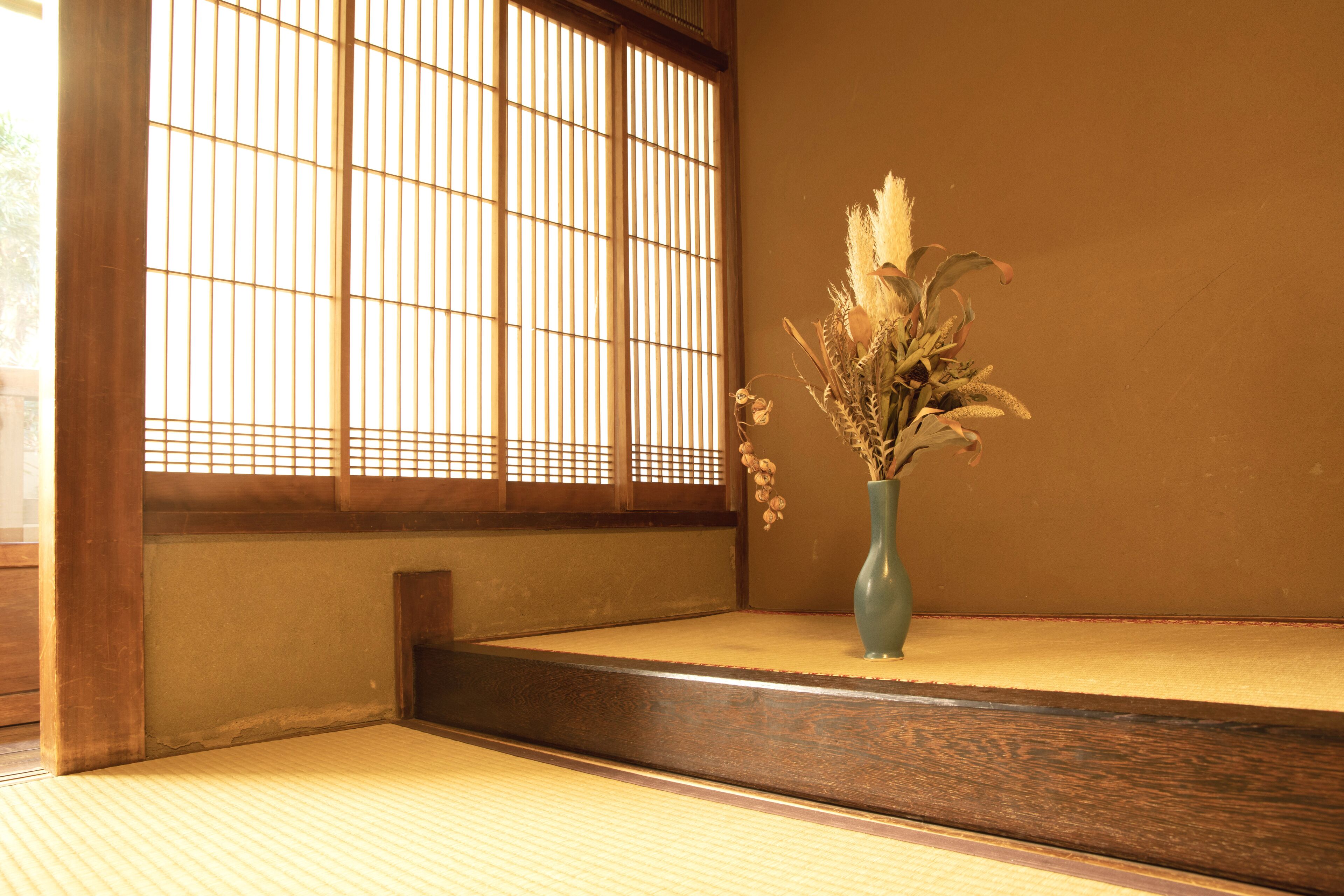 A tatami mat room with a wooden sliding door and a vase with dried flowers on a low table.
