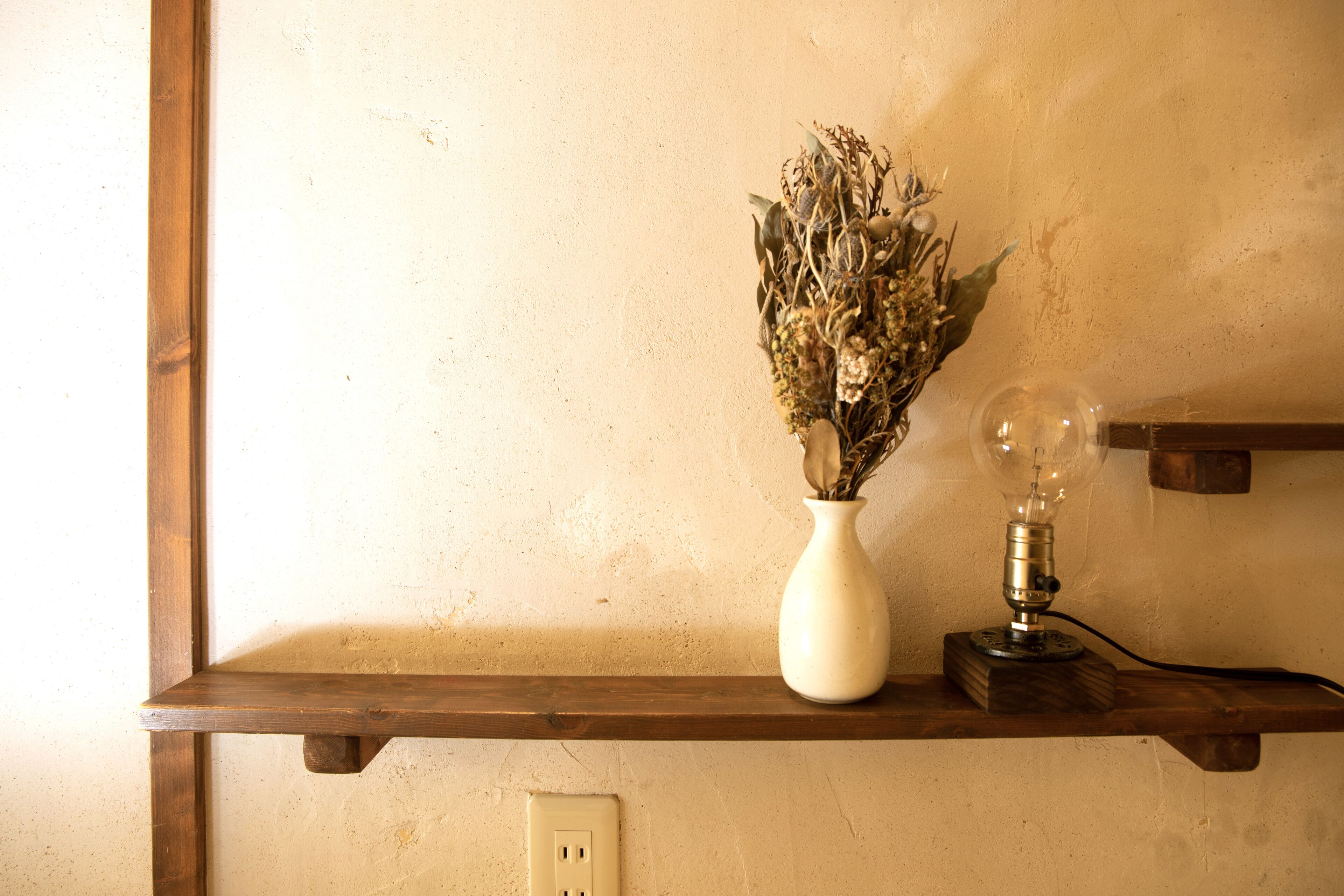 A shelf with a vase of dried flowers and a vintage-style lamp.