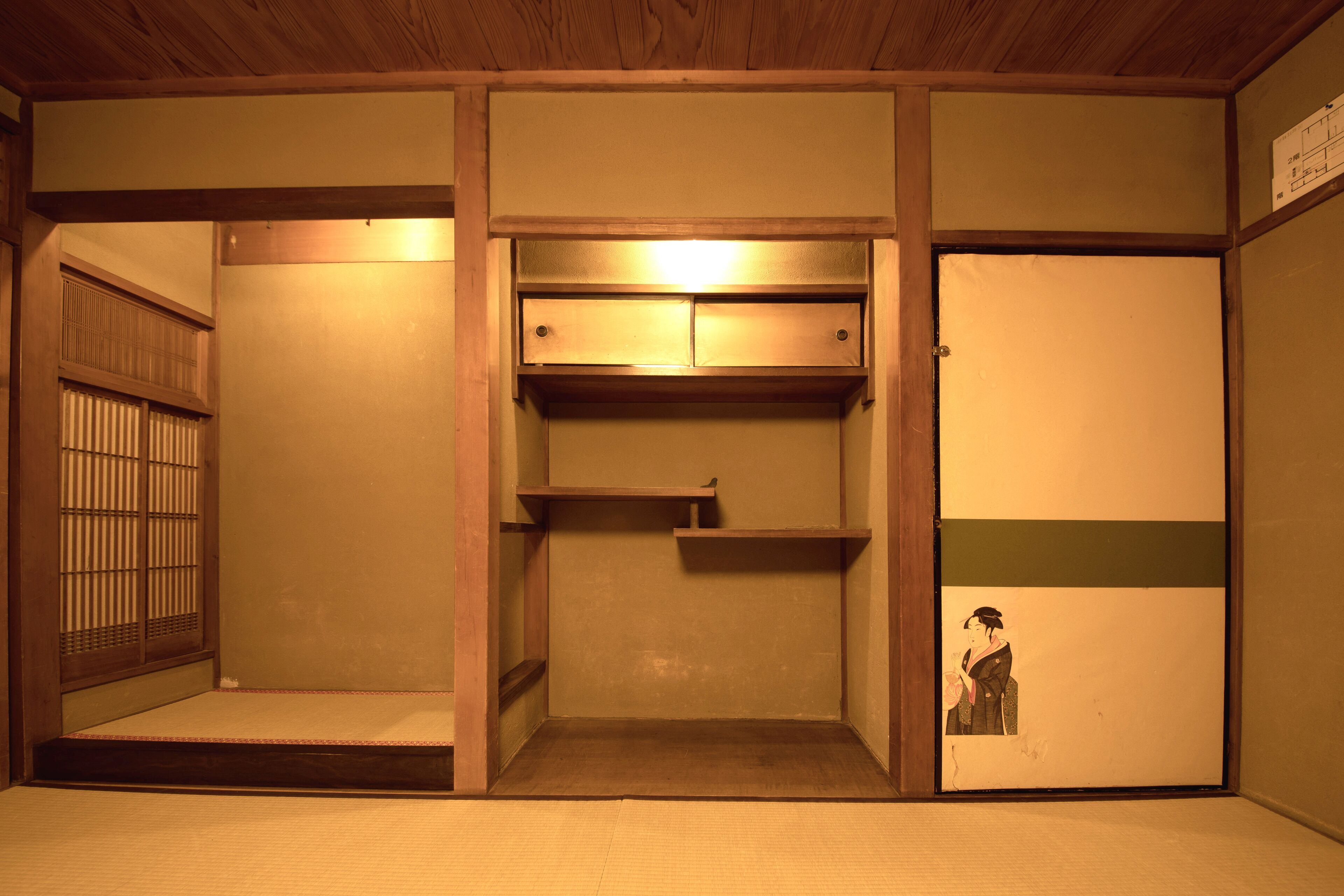 A traditional Japanese room with tatami flooring, a sliding door, a built-in shelf, and a small alcove with a picture.
