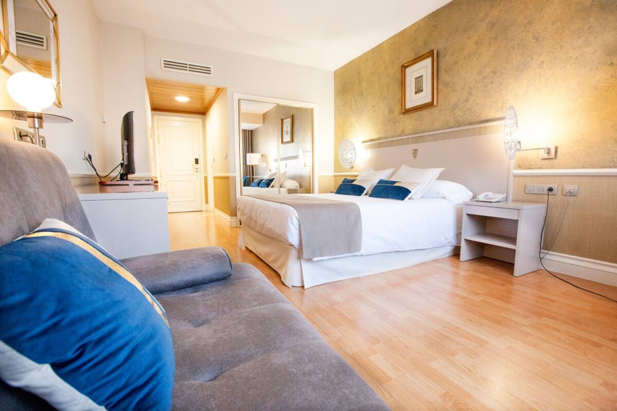 Una habitación de hotel con cama, sofá, escritorio y espejo.