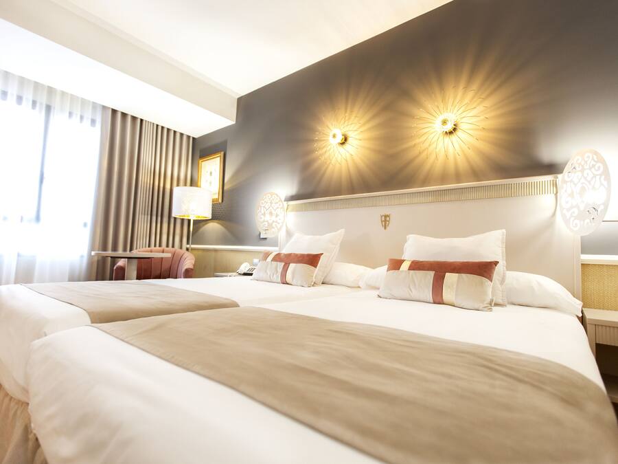 Quarto de hotel com duas camas, uma escrivaninha e uma cadeira.