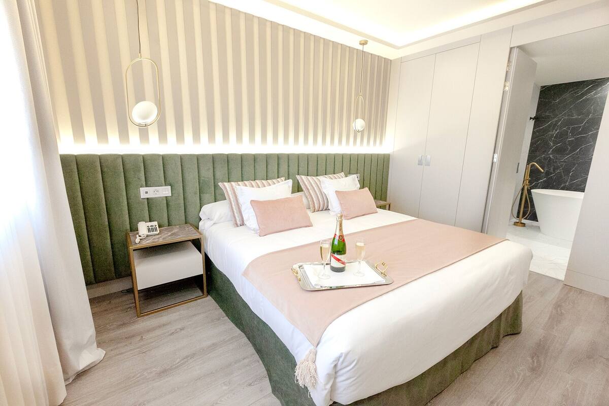 A modern hotel room with a large bed, a nightstand, a green upholstered headboard, and a bathroom with a marble wall.