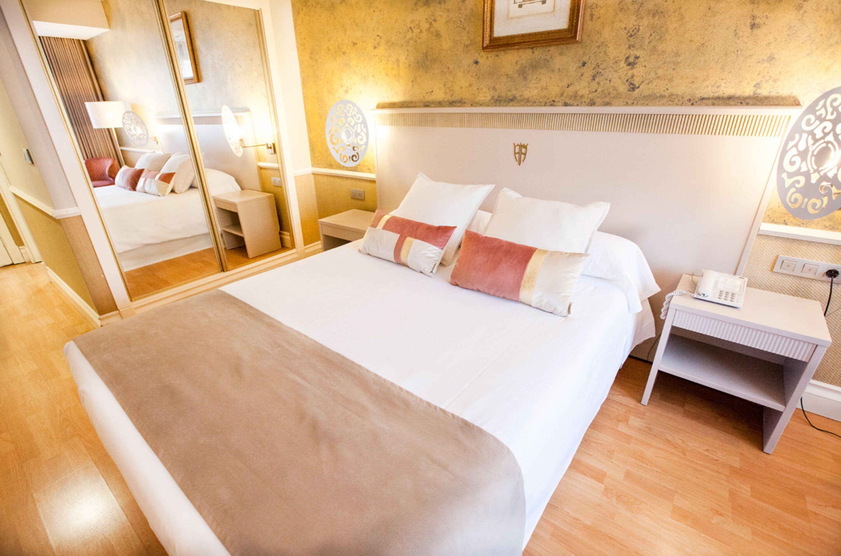 A hotel room with a large bed, bedside tables, a mirror, and a wall-mounted light fixture.