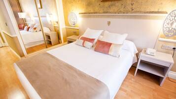 A hotel room with a large bed, bedside tables, a mirror, and a wall-mounted light fixture.