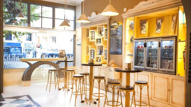A café with wooden stools, a large window, and a menu board. - Alfonso VIII (Soria)