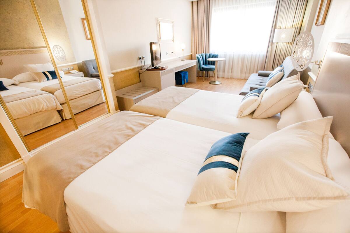 Habitación de hotel con dos camas, un escritorio, una silla y una mesita.