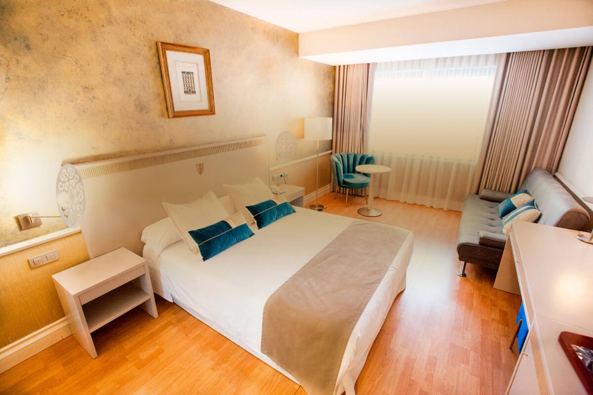Una habitación de hotel con una cama grande, mesitas de noche, un escritorio, una silla y una ventana con cortinas.