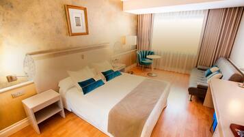 A hotel room with a large bed, bedside tables, a desk, a chair, and a window with curtains.
