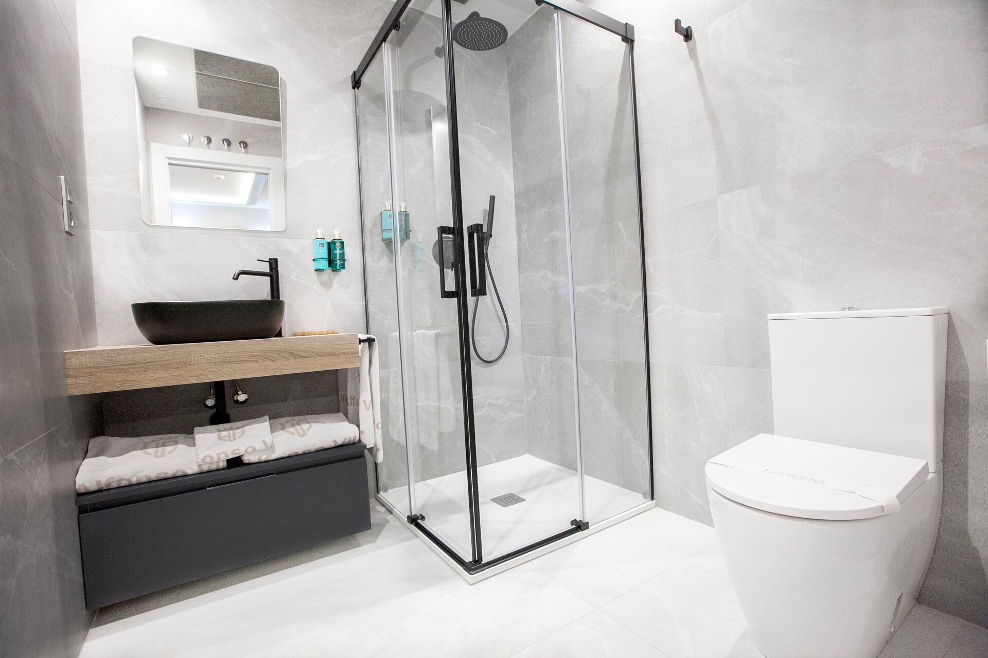 A modern bathroom with a glass-enclosed shower, a black sink, and a white toilet.