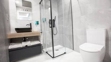 A modern bathroom with a glass-enclosed shower, a black sink, and a white toilet.