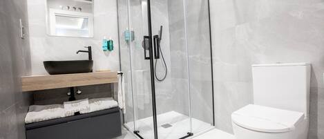A modern bathroom with a glass-enclosed shower, a black sink, and a white toilet.