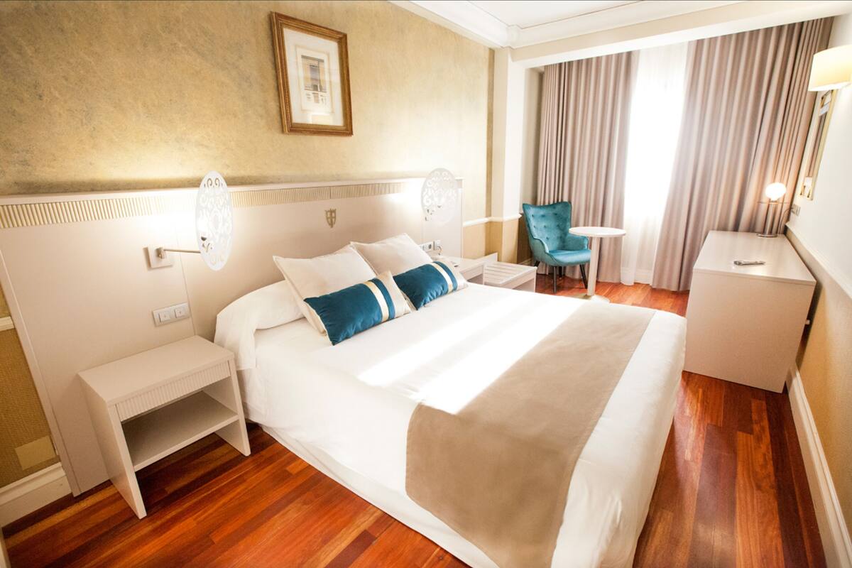 Una habitación de hotel con una cama grande, mesitas de noche, una silla y un escritorio.