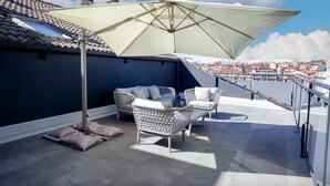 A rooftop terrace with a large umbrella, two wicker chairs, and a view of the city. - Alfonso VIII (Soria)