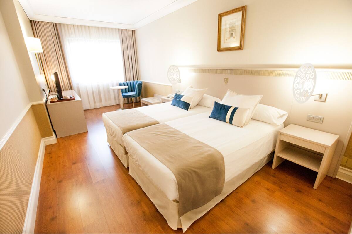 Una habitación de hotel con una cama grande, dos mesitas de noche, una silla, un escritorio y una lámpara.