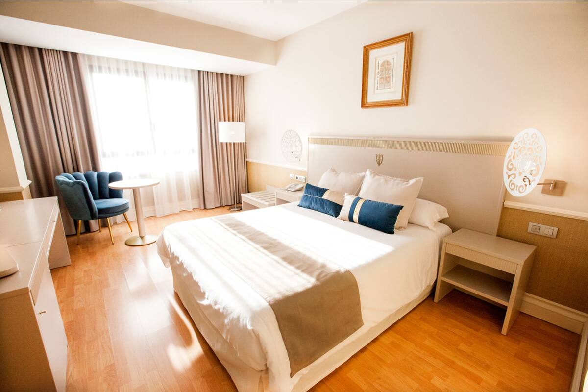 Una habitación de hotel con una cama grande, mesitas de noche, un escritorio y una silla.