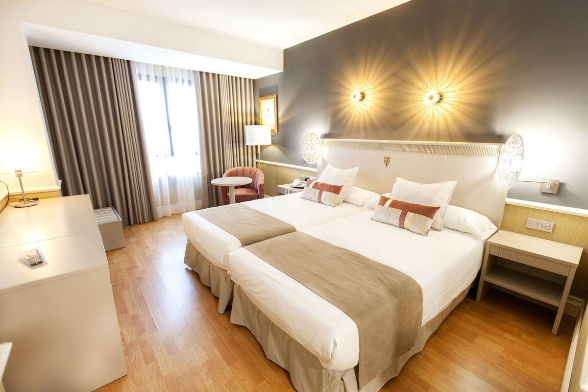 Habitación de hotel con dos camas, un escritorio, una silla, una lámpara y una lámpara de pared.