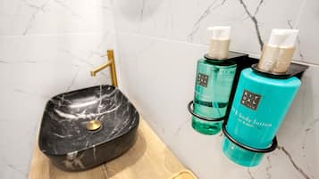 A bathroom with a marble sink, a gold faucet, and two bottles of body lotion on a wooden shelf.