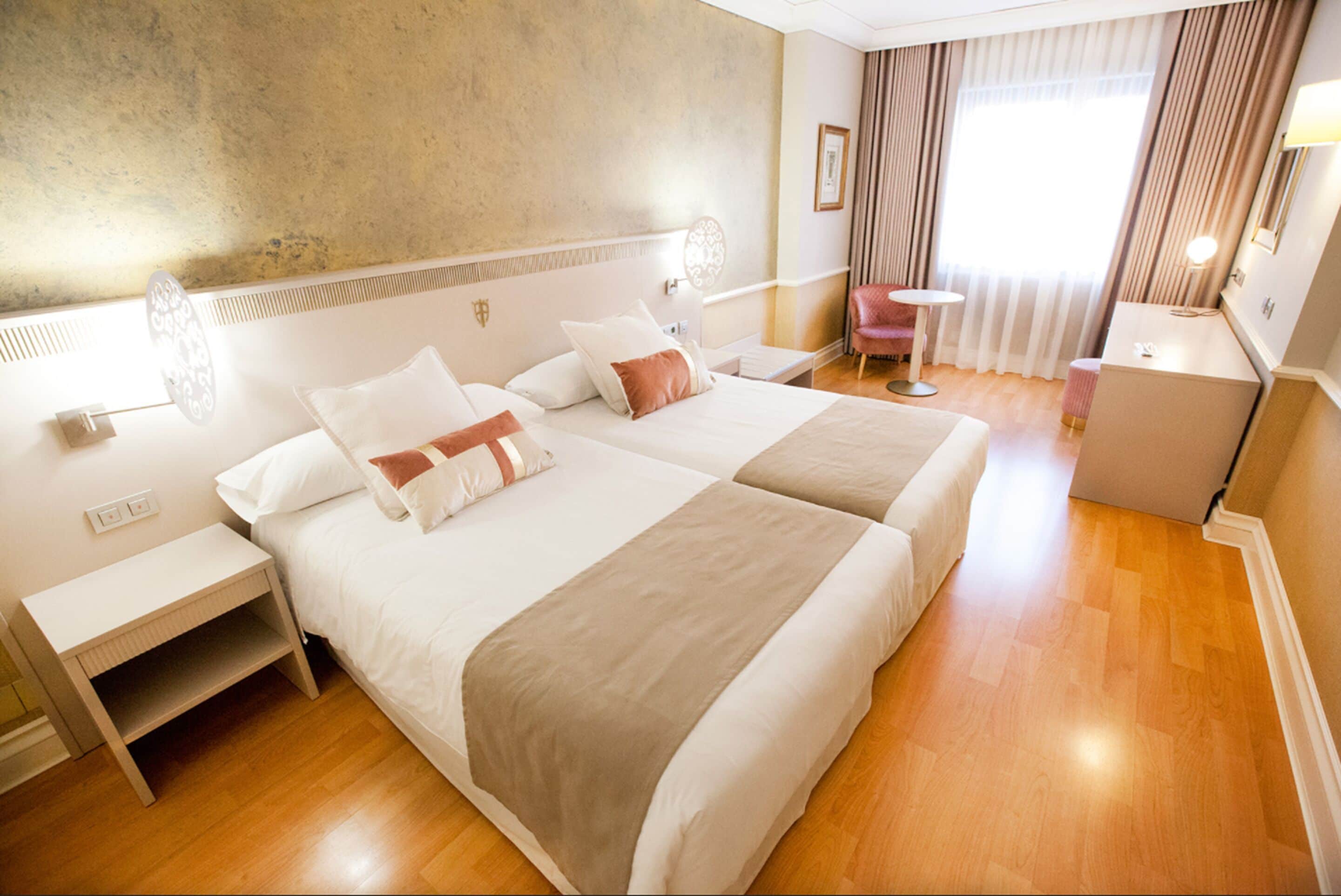 Ein Hotelzimmer mit zwei Betten, einem Schreibtisch, einem Sessel und einem kleinen Tisch.