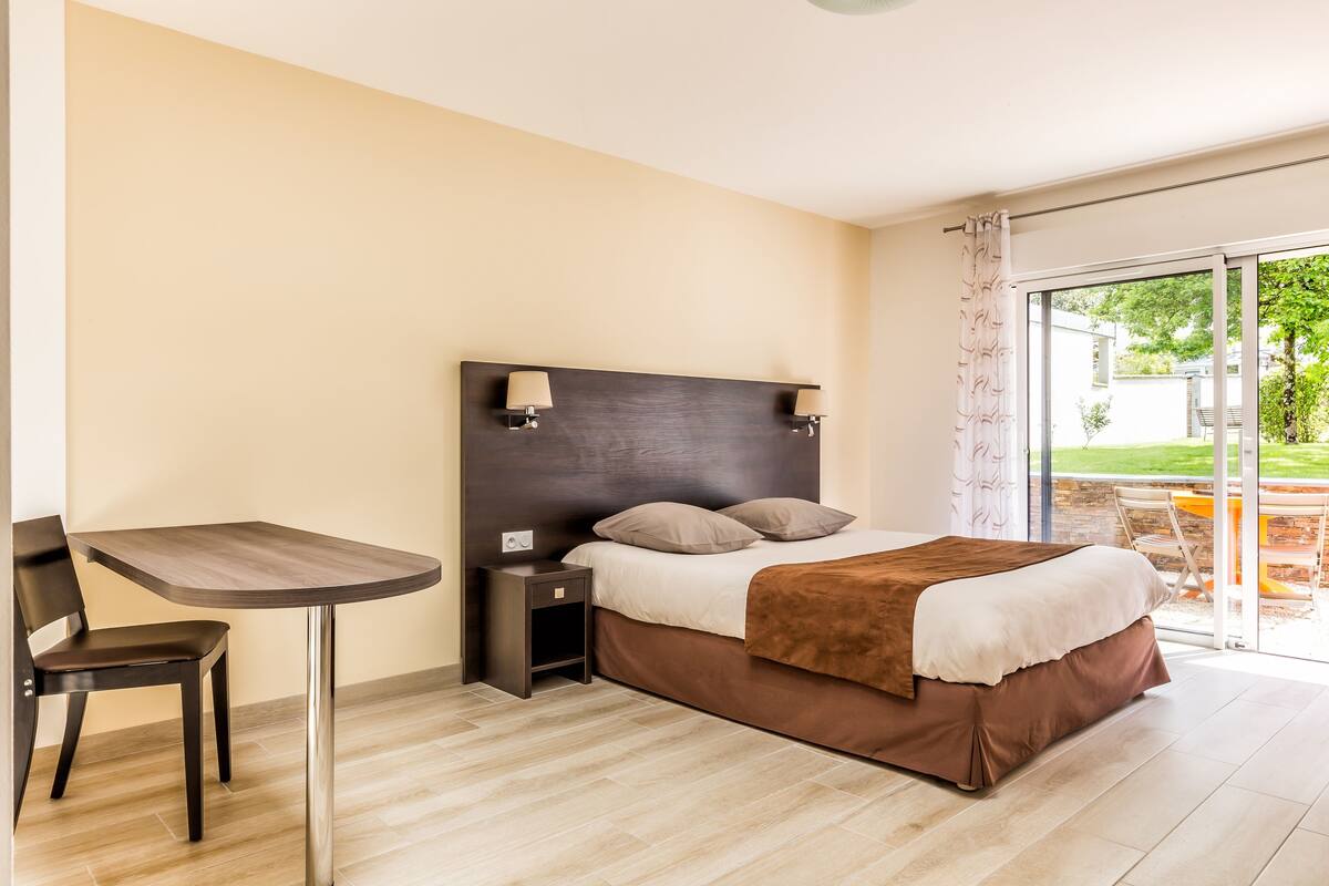 A hotel room with a bed, a small table, and a chair.