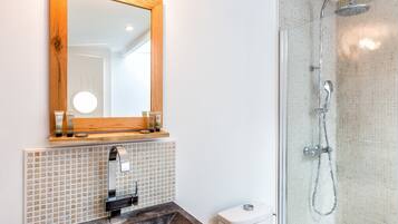 A bathroom with a wooden-framed mirror, a tiled backsplash, a sink with a dark countertop, and a glass-enclosed shower with a handheld showerhead.