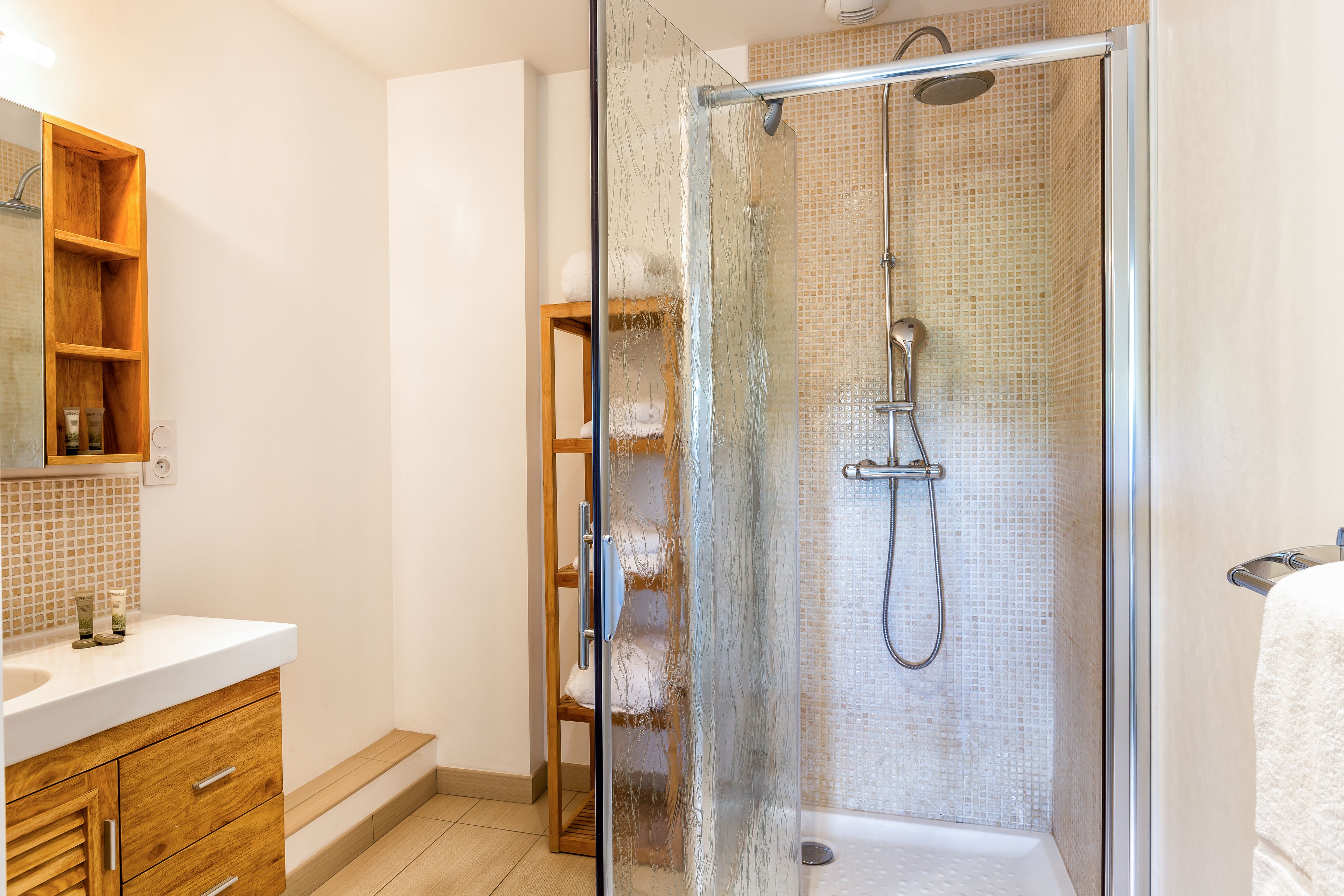 A modern bathroom with a glass-enclosed shower, a wooden vanity, and a tiled shower wall.