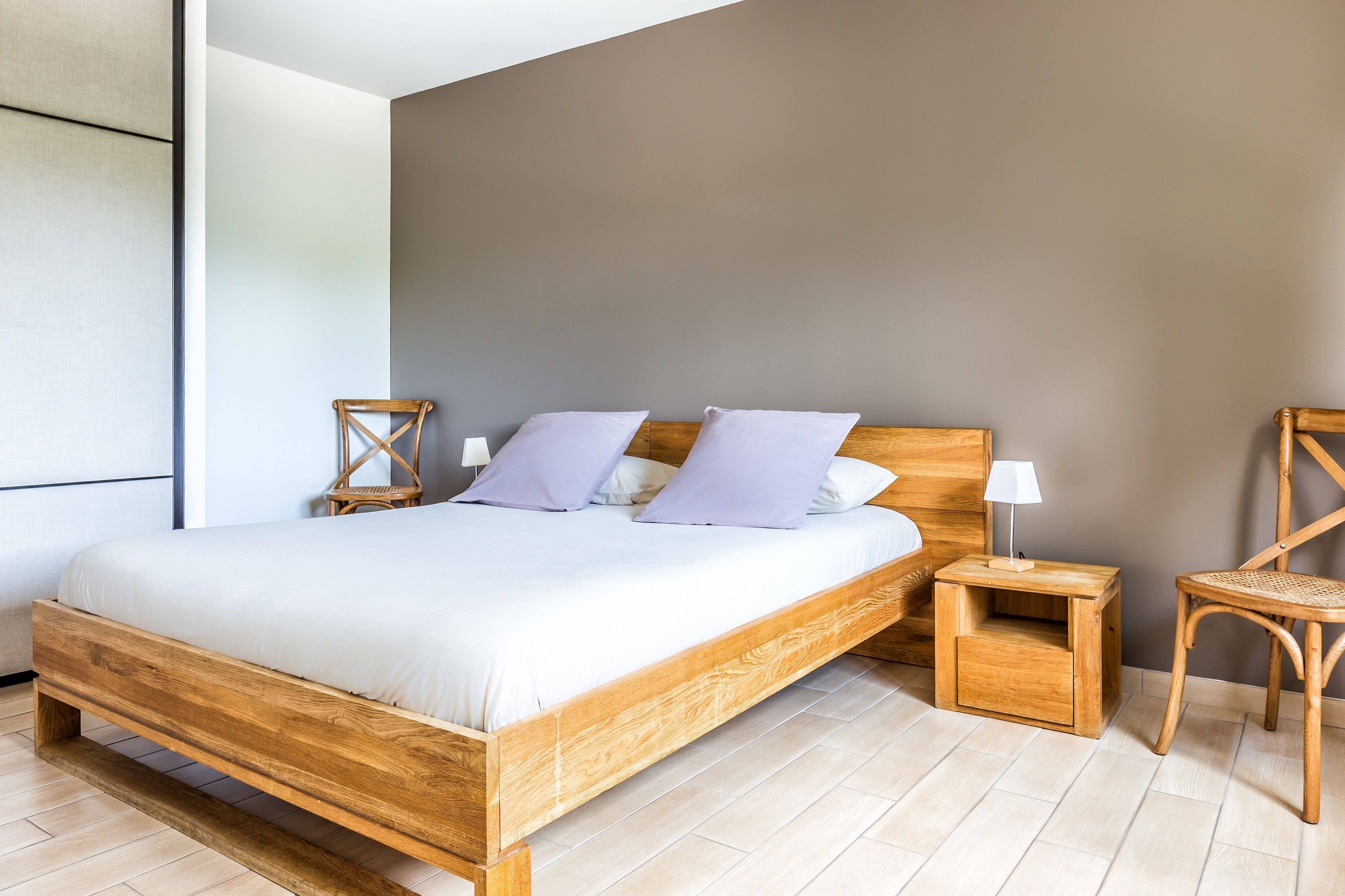 A modern bedroom with a wooden bed, two nightstands, a wicker chair, and a large window.