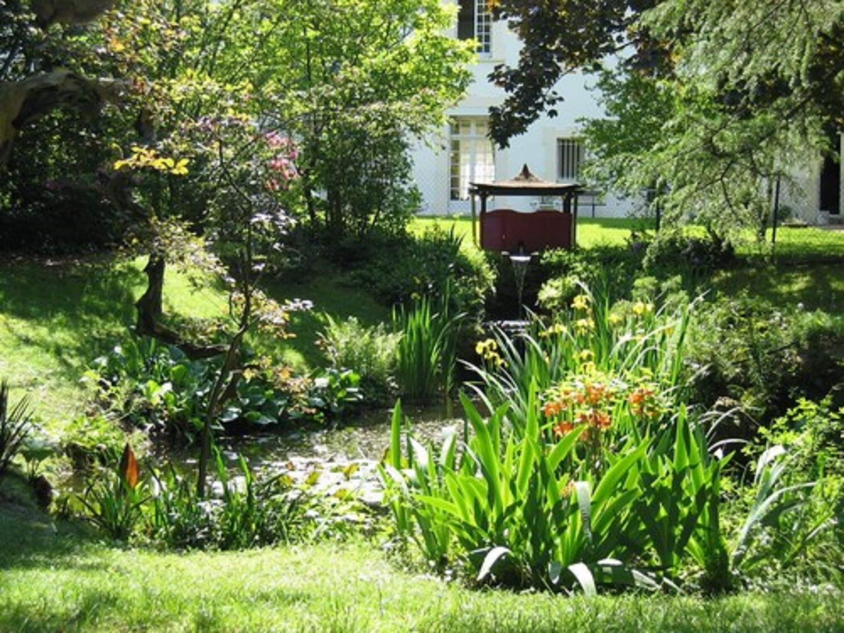 En frodig trädgård med en lusthus, en damm och ett stort utbud av växter och blommor.