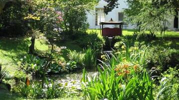 En frodig trädgård med en lusthus, en damm och ett stort utbud av växter och blommor.