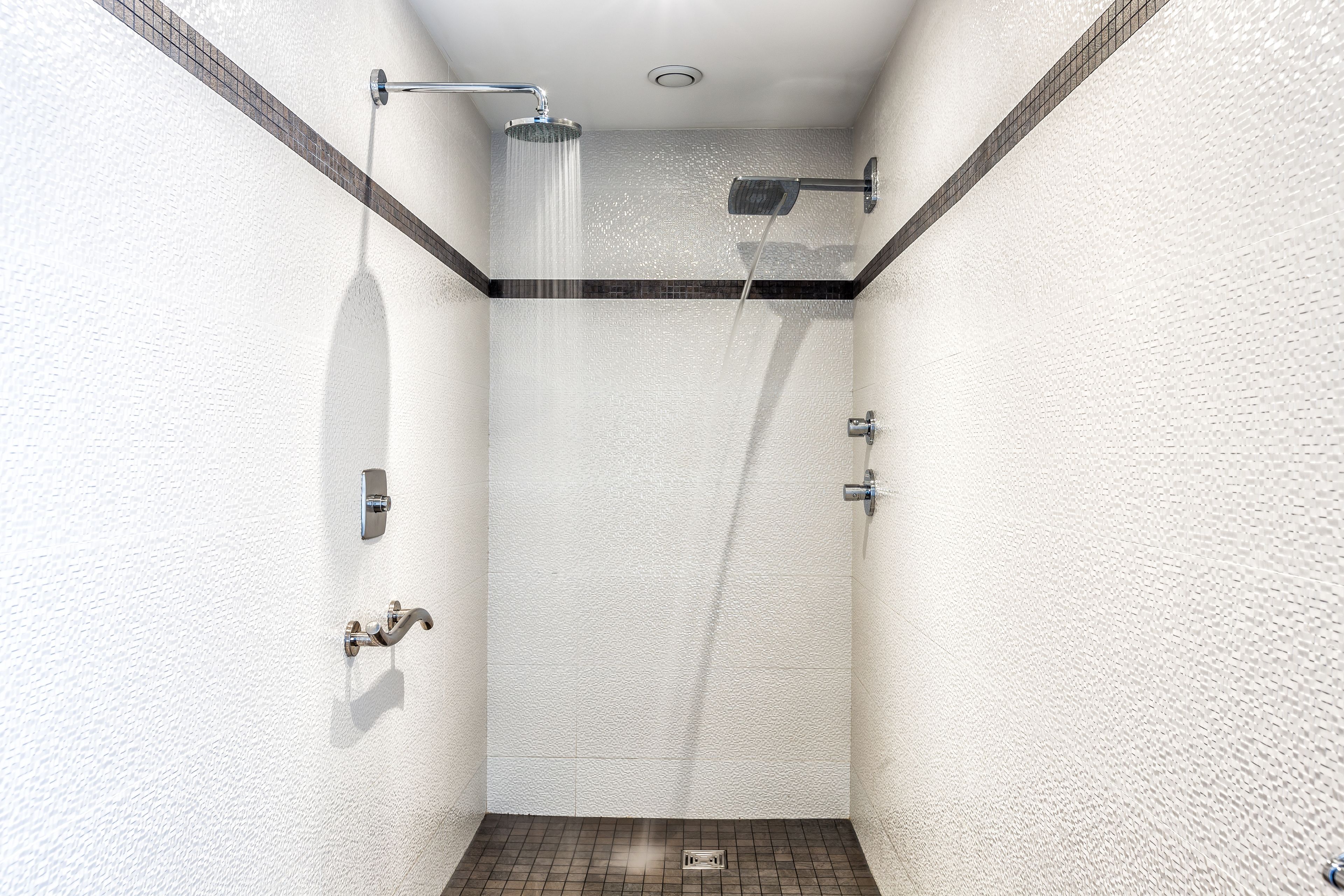 A modern shower with a rain showerhead, a handheld showerhead, and a wall-mounted faucet.