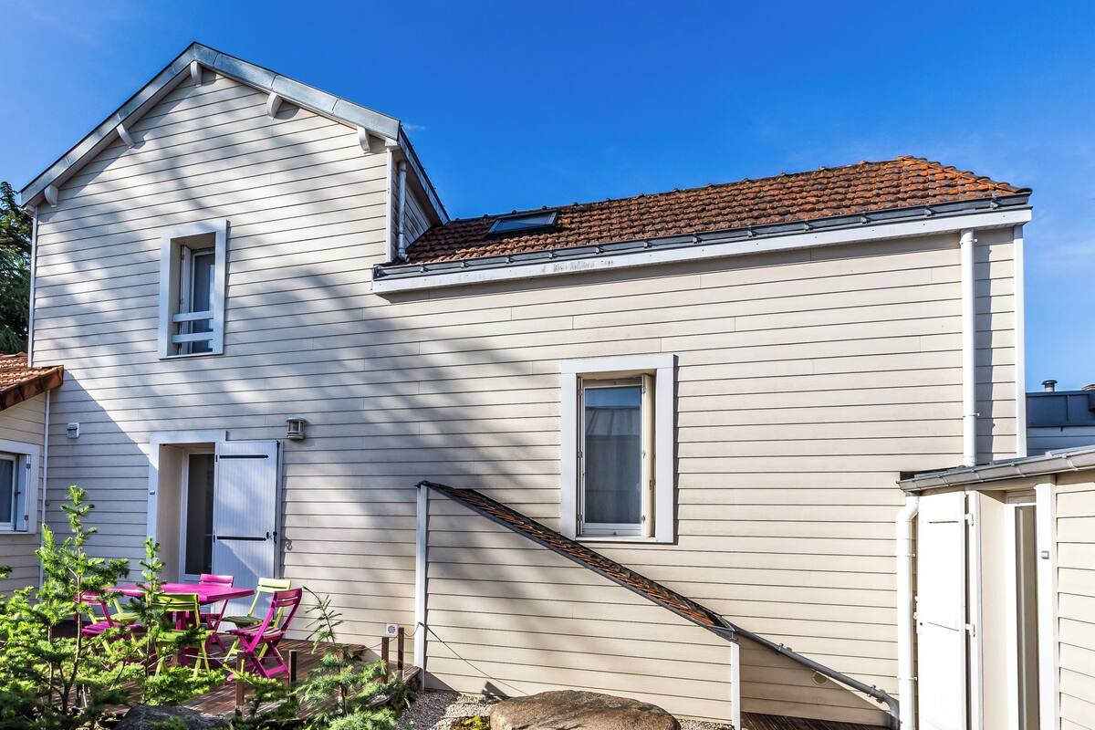 A two-story house with a tiled roof, a front door, and a small porch with a table and chairs.