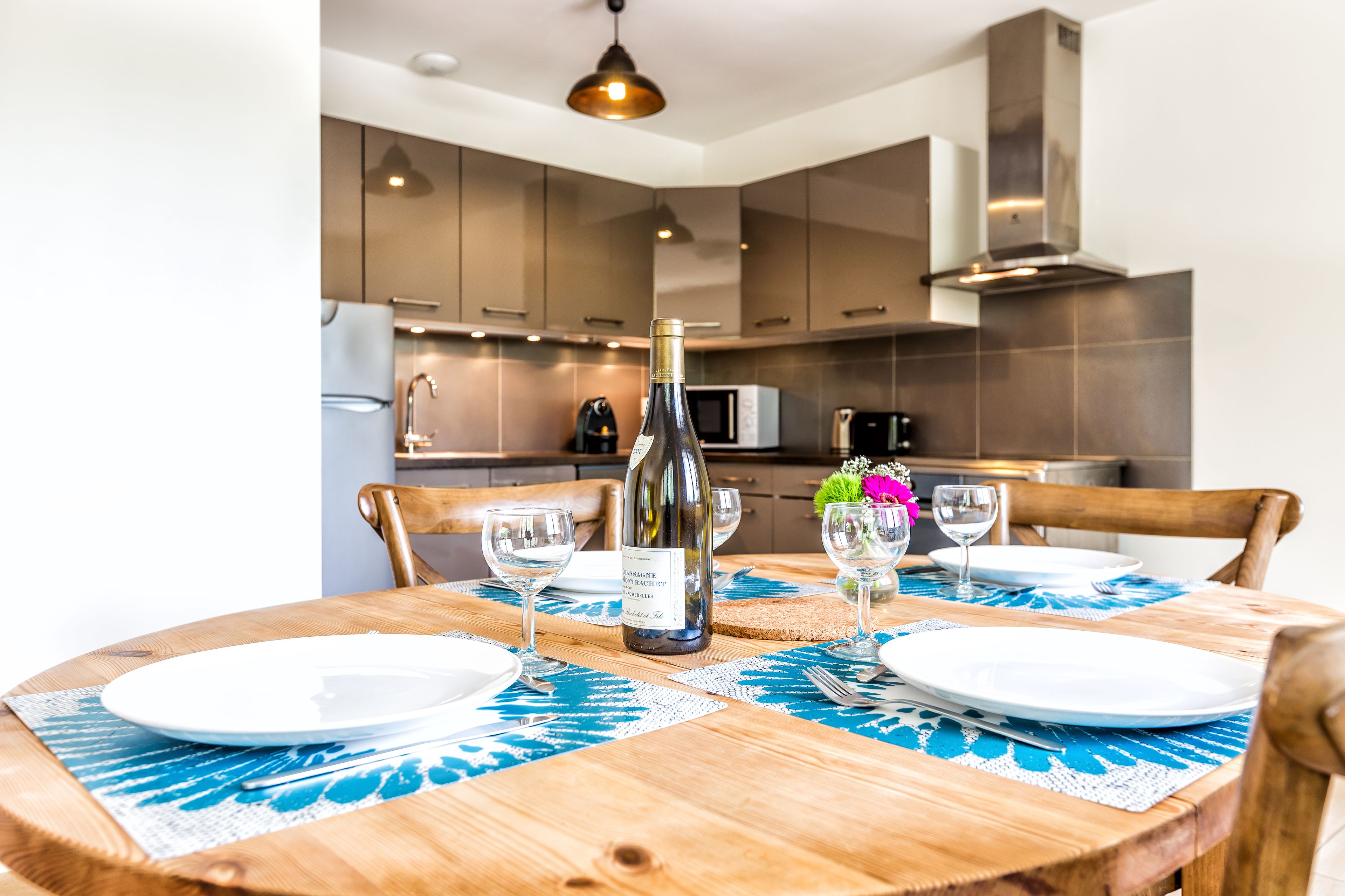Une table à manger dressée avec des assiettes, des verres et une bouteille de vin, entourée de chaises en bois.