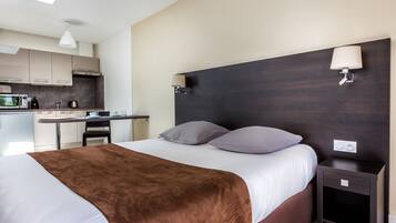 A hotel room with a bed, bedside table, and a view of the kitchen.