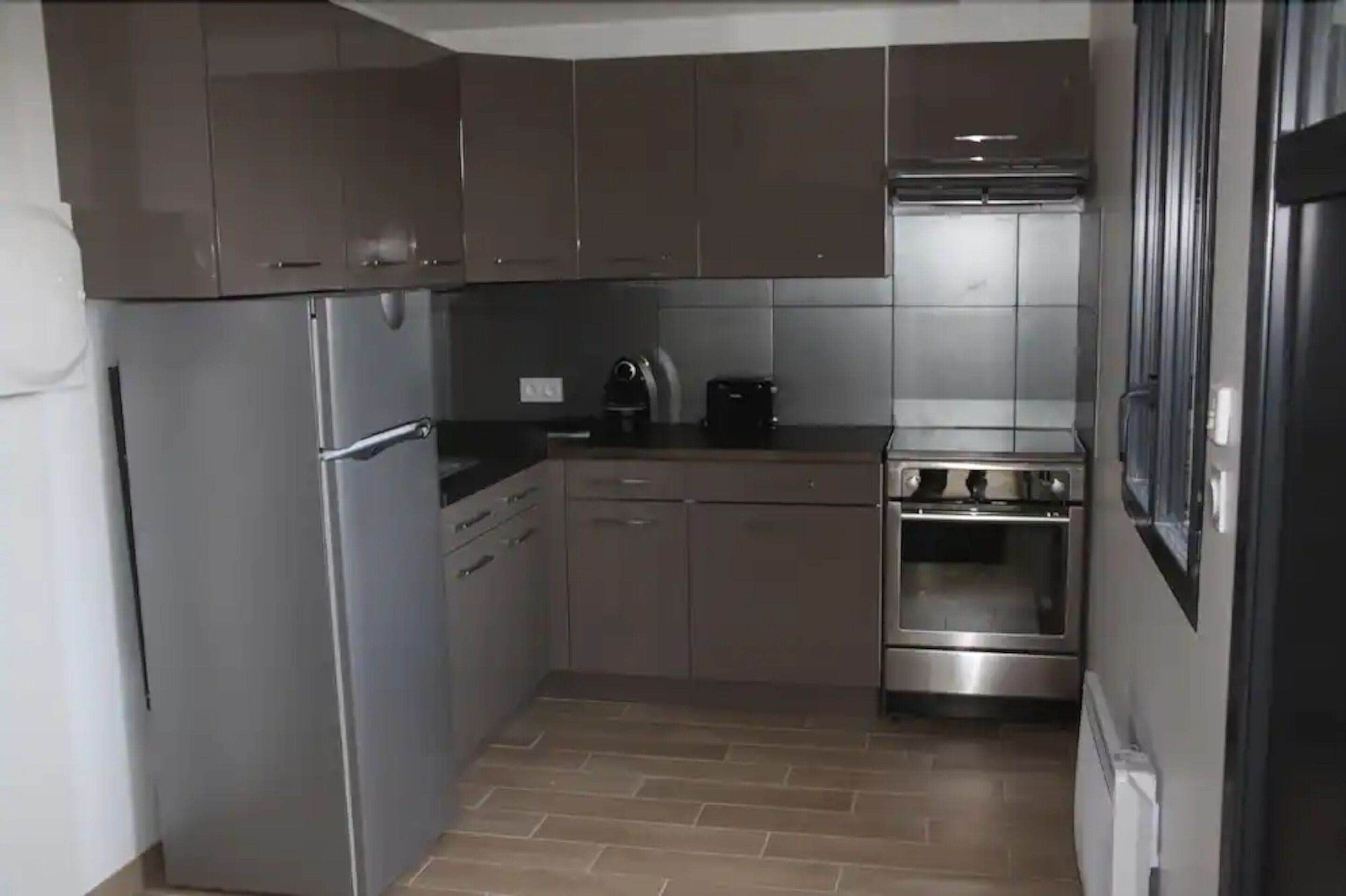 Een compacte keuken met roestvrijstalen apparatuur, waaronder een koelkast, oven en koffiezetapparaat.