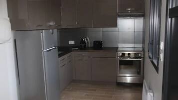 Een compacte keuken met roestvrijstalen apparatuur, waaronder een koelkast, oven en koffiezetapparaat.