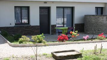Un edificio moderno con un patio de grava, un pequeño jardín con flores coloridas y un banco de piedra.