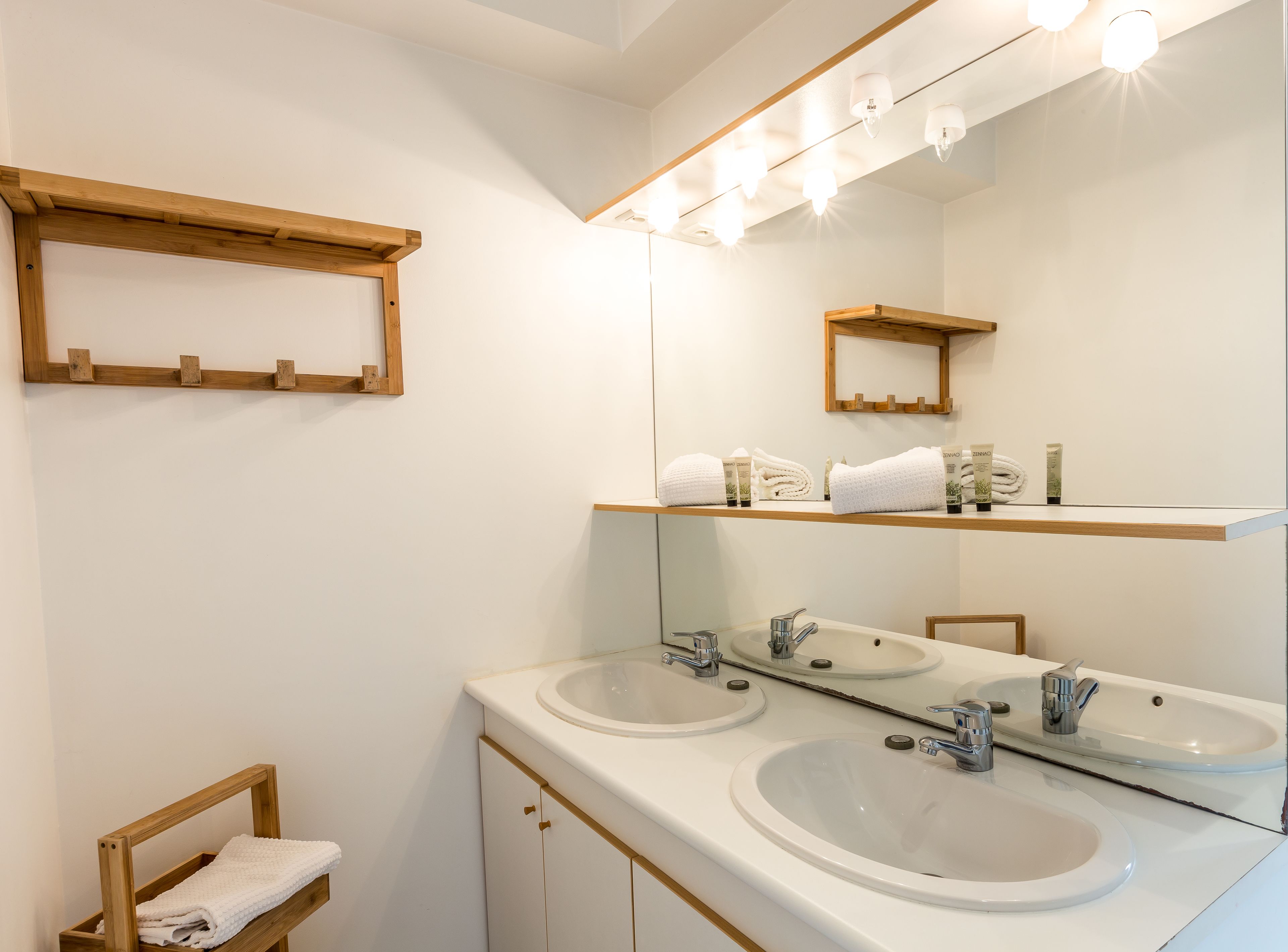 A bathroom with two sinks, a mirror, and a shelf with toiletries.