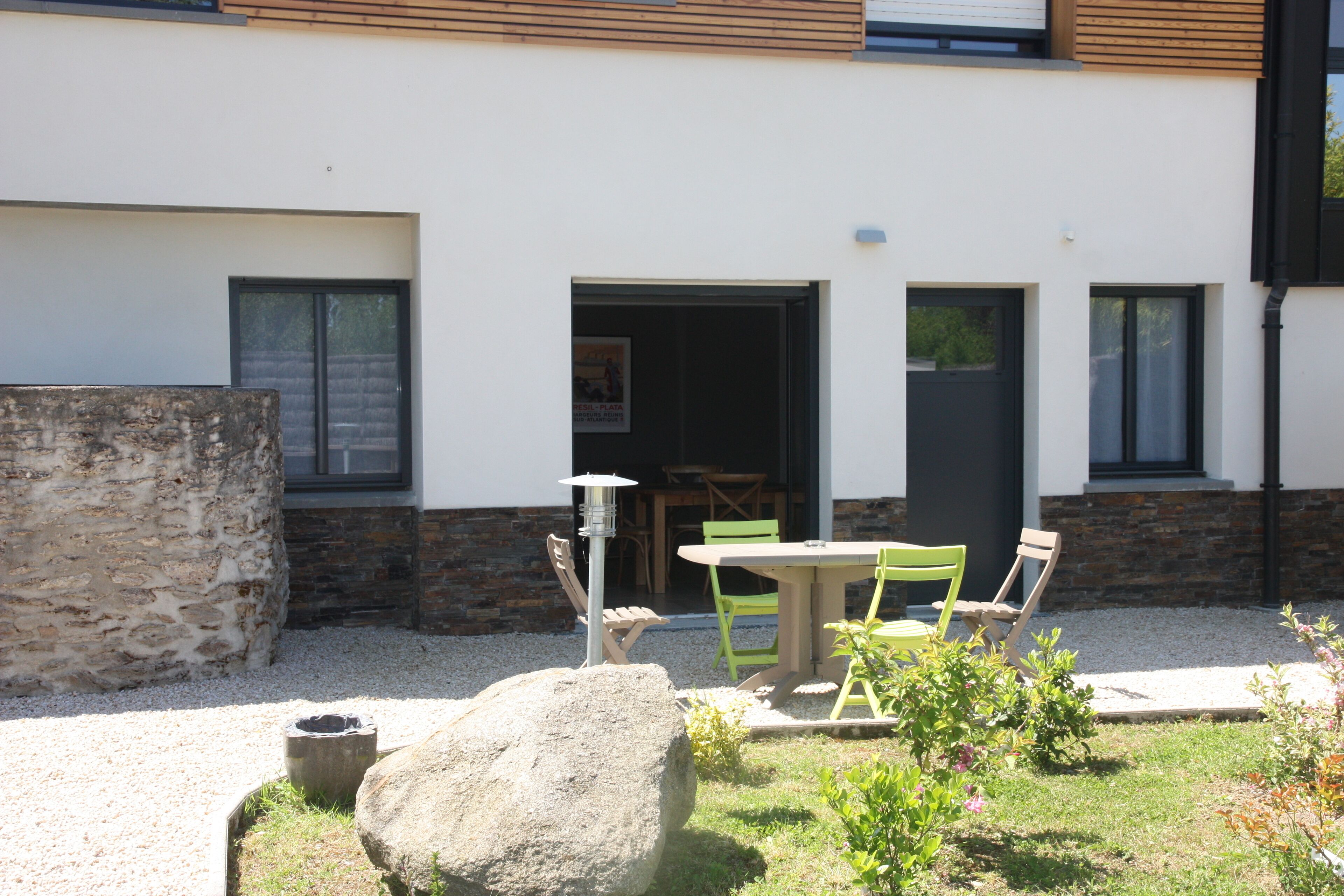 Een modern gebouw met een stenen muur, een patio met grind en een tafel met stoelen.