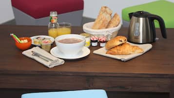 A breakfast table with bread, croissants, a coffee pot, a bottle of orange juice, and a bowl of cereal.