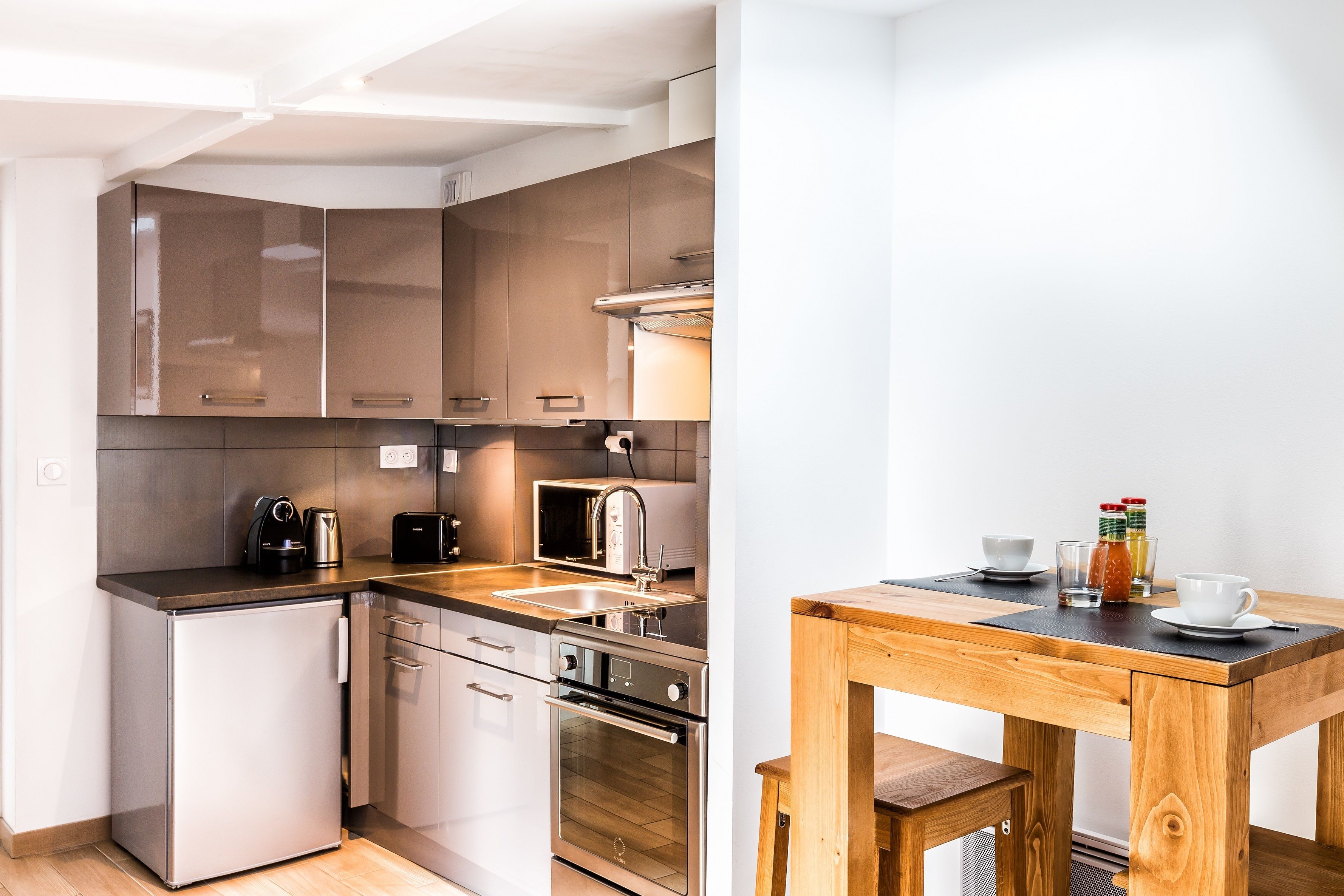 A compact kitchen with stainless steel appliances, a wooden table, and a small refrigerator.