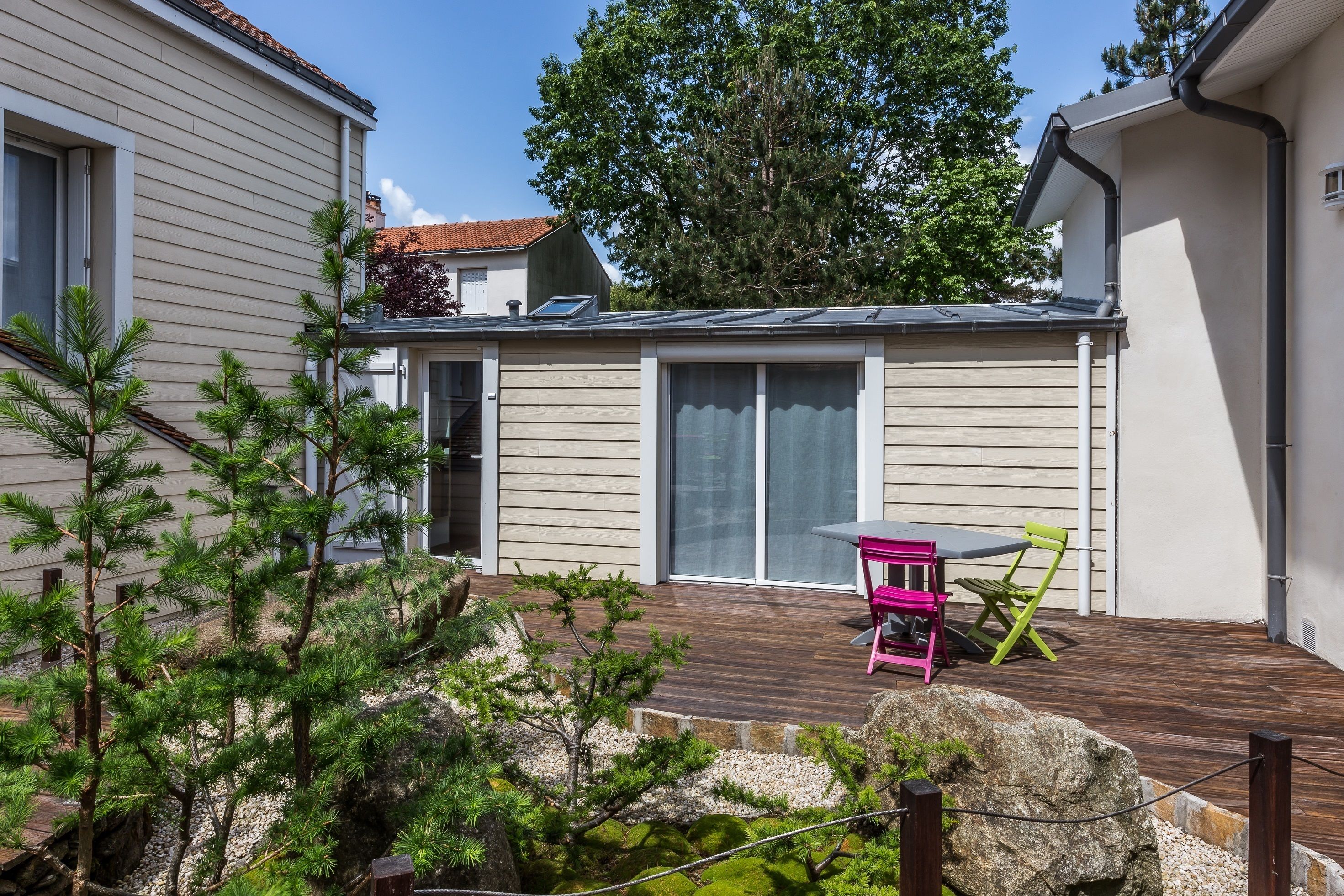 Et hus med en træterrasse, en skydedør og en lille terrasse med et bord og stole.