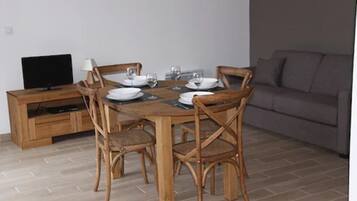 A dining area with a wooden table set for four, surrounded by wicker chairs. A television is on a wooden cabinet to the left.