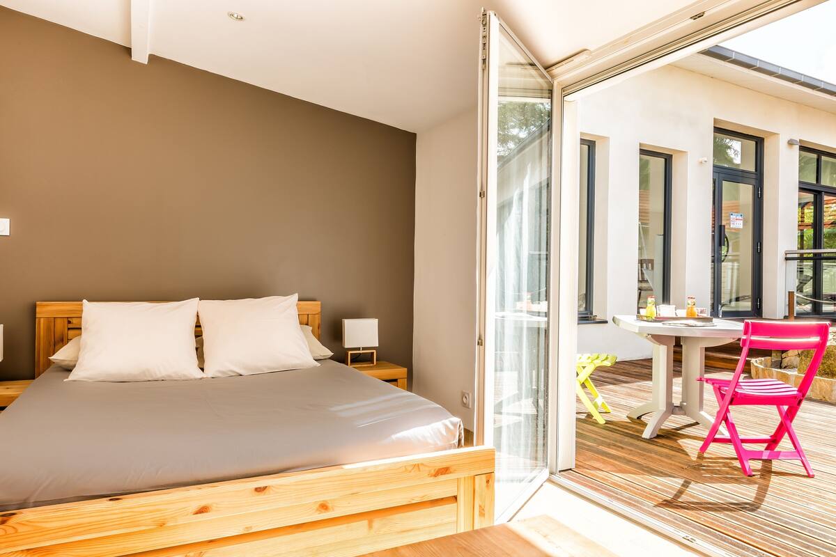 A bedroom with a wooden bed, a bedside table, and a glass door leading to an outdoor area with a table and chairs.