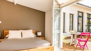 A bedroom with a wooden bed, a bedside table, and a glass door leading to an outdoor area with a table and chairs.