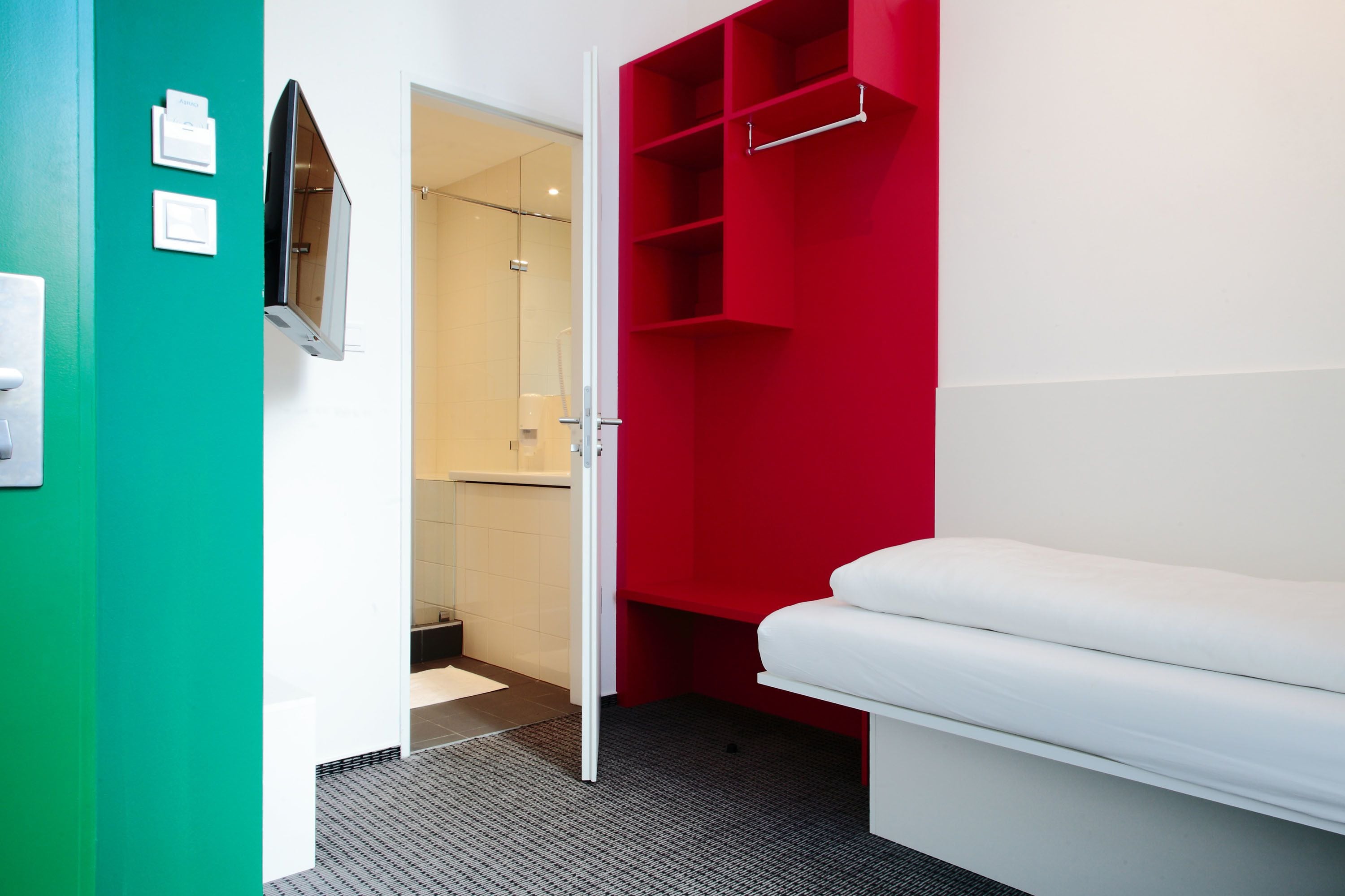 Een moderne hotelkamer met een wit bed, een rode garderobe en een douchecabine van glas.