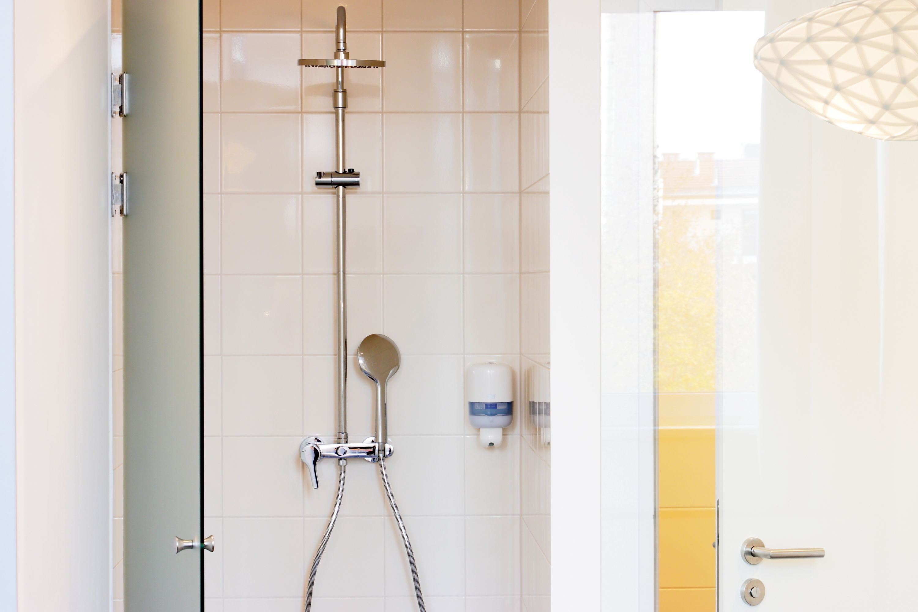 Eine Dusche mit Duschbrause, Seifenspender an der Wand und einer Tür mit Griff.