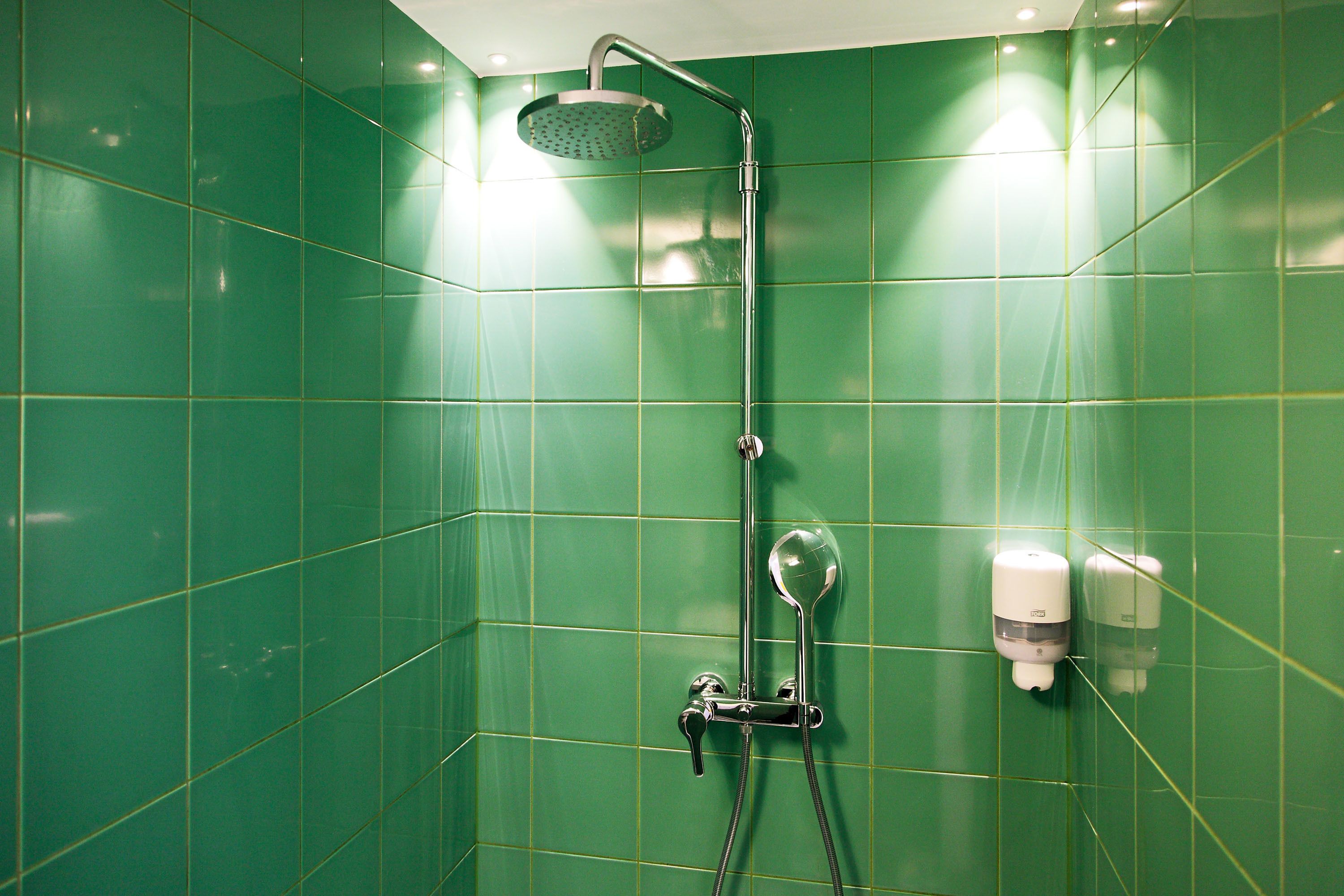 Une salle de bain avec des carreaux verts, une pomme de douche, un pommeau de douche amovible et un distributeur de savon.