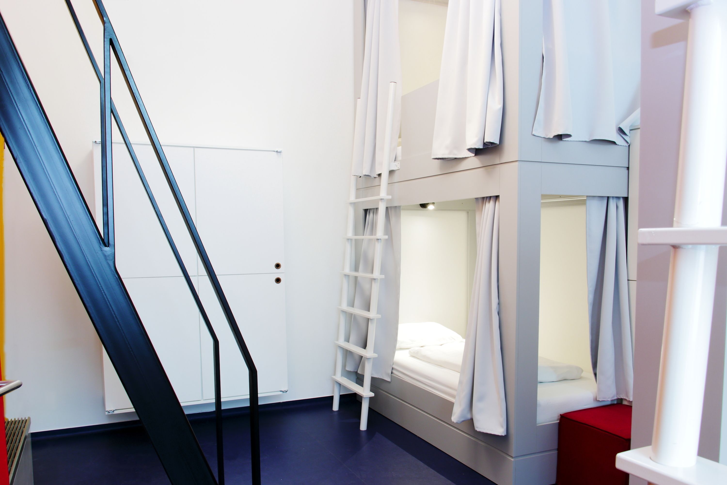 Dormitorio con literas, una escalera, una puerta blanca y un banco rojo.
